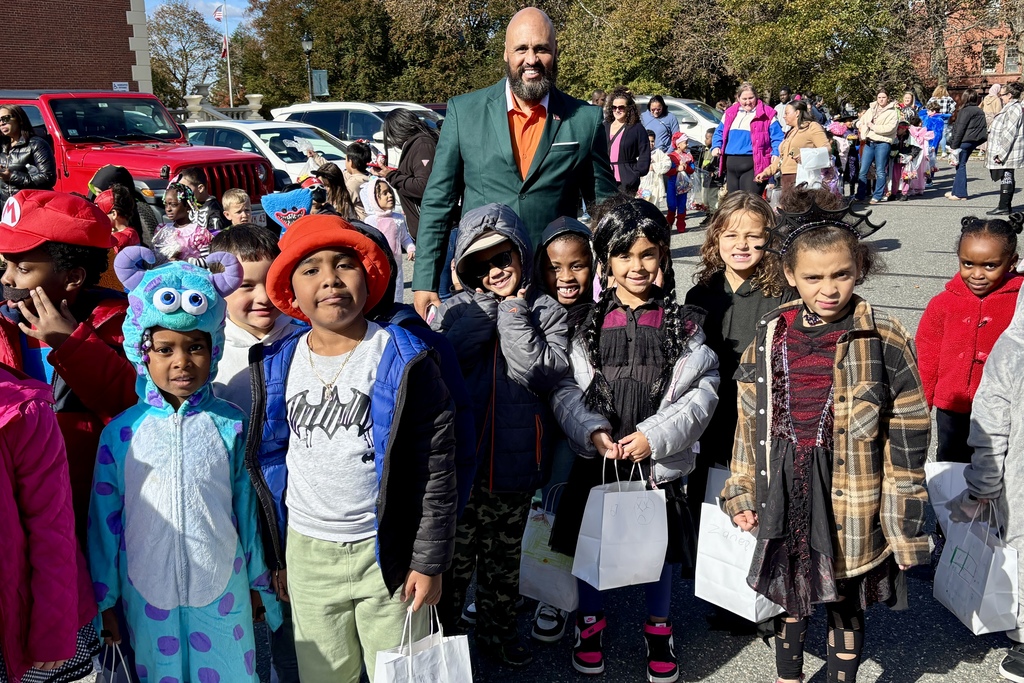 A group of children in costumes pose with an adult on a sunny day.