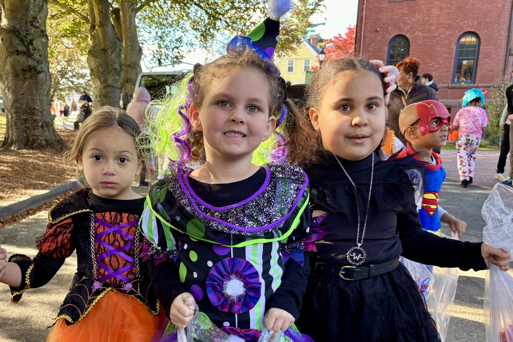 Three children in Halloween costumes pose for a photo outdoors.