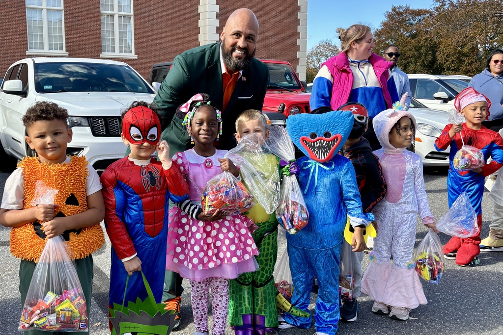 Children in costumes pose with a smiling adult, holding bags of candy.