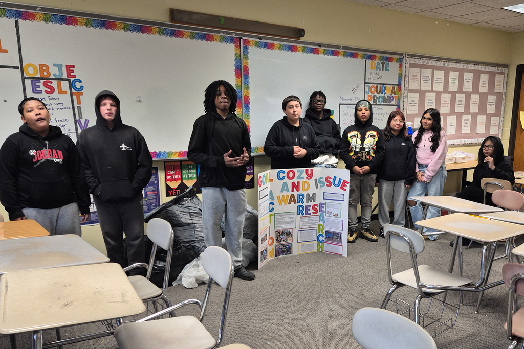 Students pose for a photo, standing alongside a poster board with details about their civics action project. 