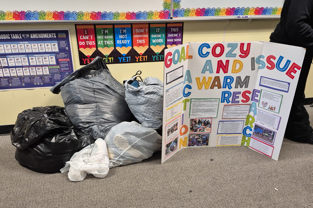 Bags of clothes are laid alongside a posterboard with details about a class civics action project.