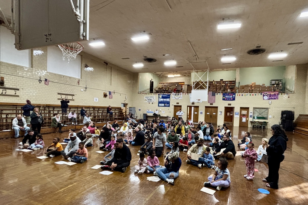A large group of people, including children, gather in a gymnasium.