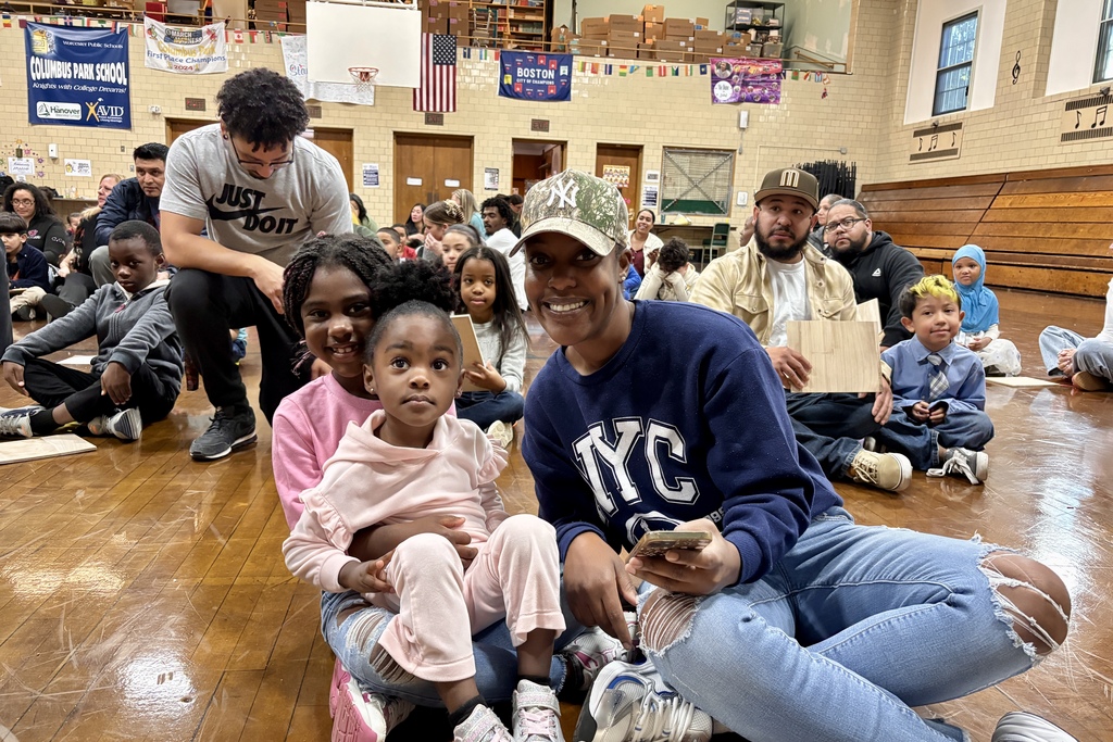 A group of people, including children, gather in a school gymnasium.