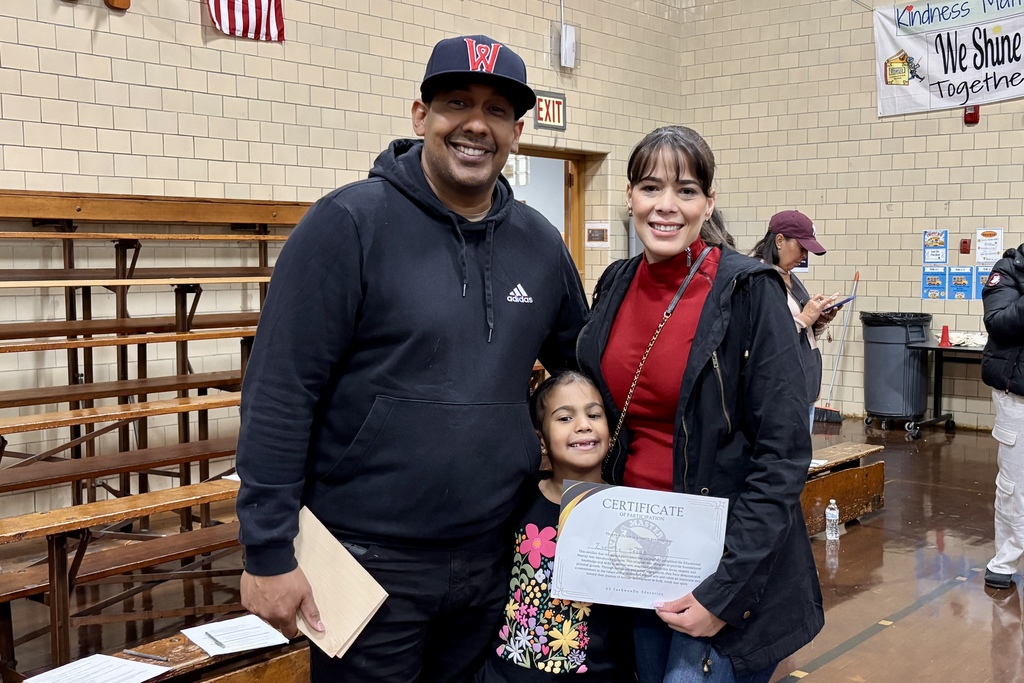 A family smiles for the camera, holding a certificate in a school setting.