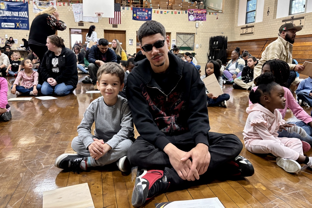 A man and a young boy sit on the floor, smiling at the camera.