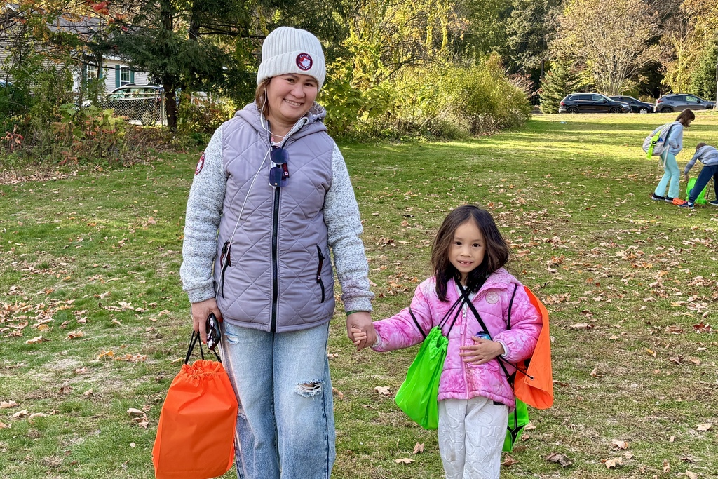 A woman and a young girl hold hands, smiling in a park on a sunny day.