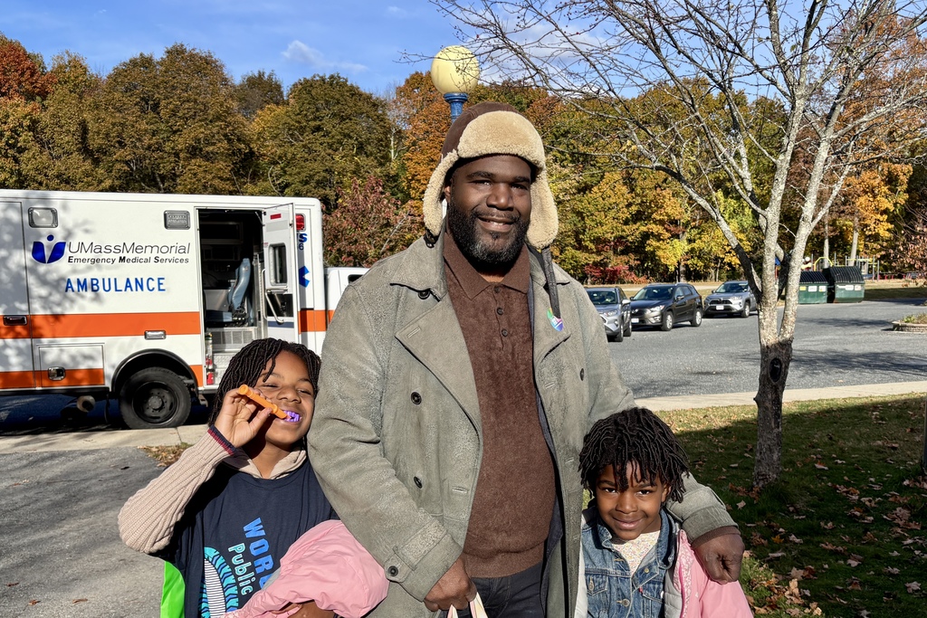 A man and two children smile in front of an ambulance on a sunny day.