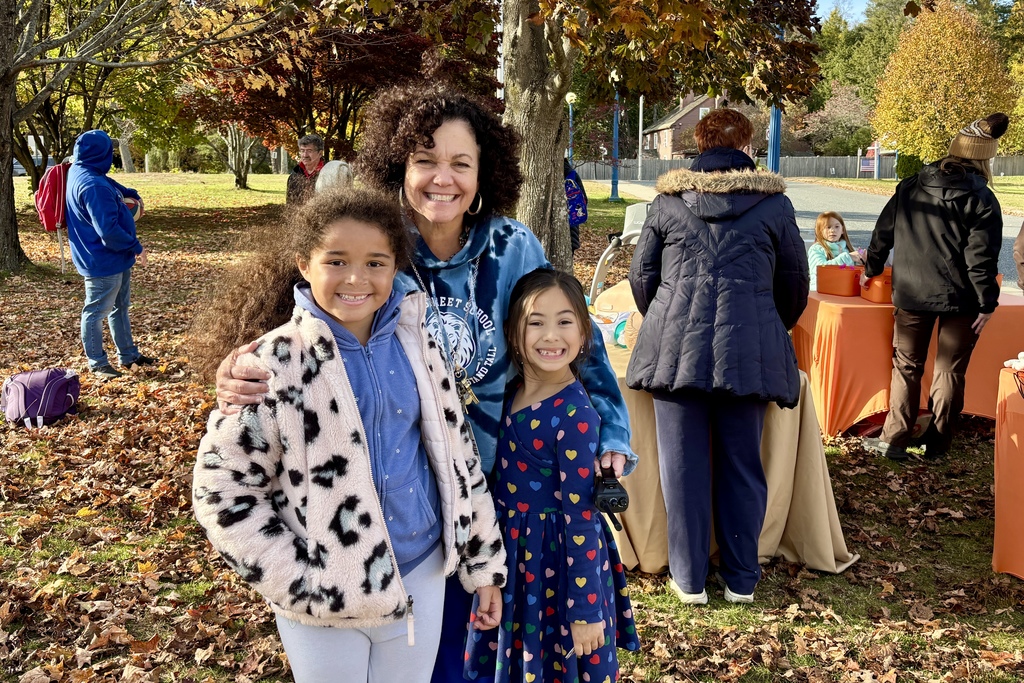A woman and two girls smile for the camera outdoors on a sunny day.