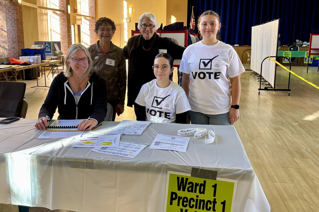 Volunteers at a polling place stand behind a table, ready to assist voters.