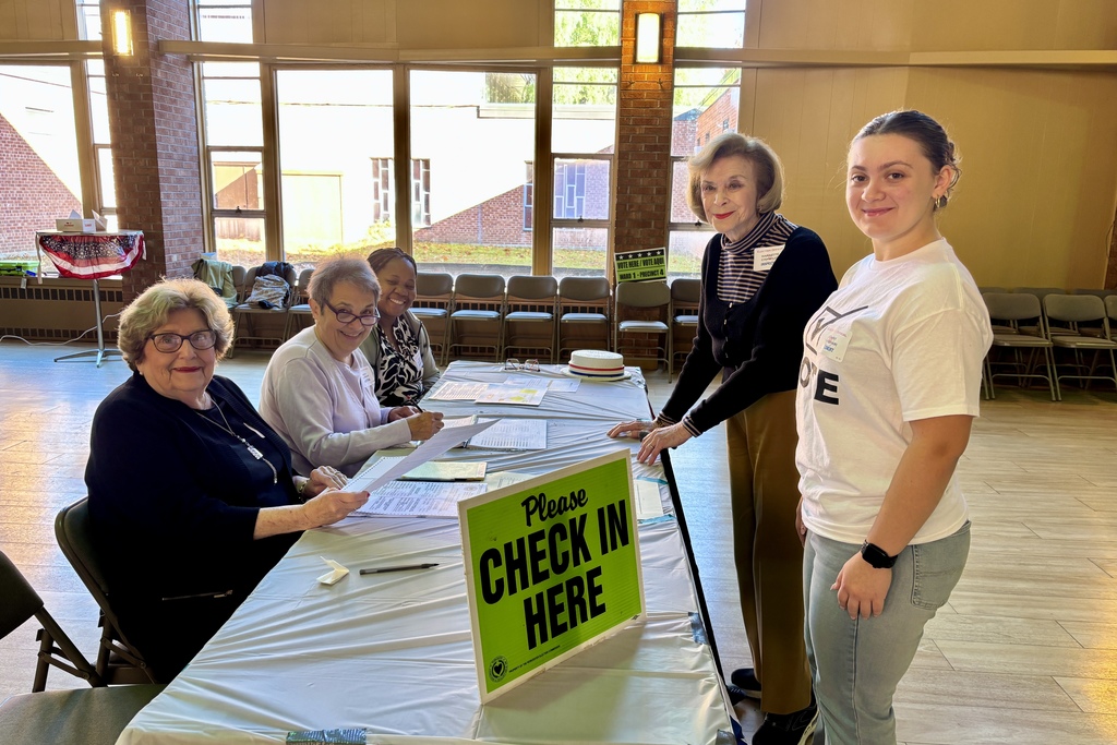People check in at a polling place, with a sign that says 'Check In Here'.