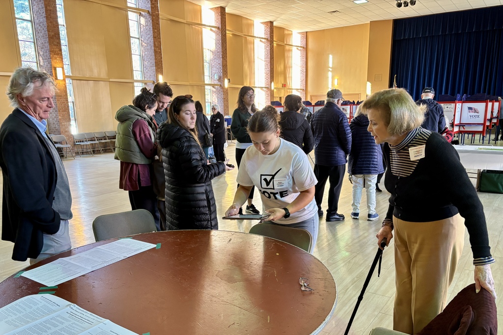 People gather at a polling place, some reviewing documents at a table.