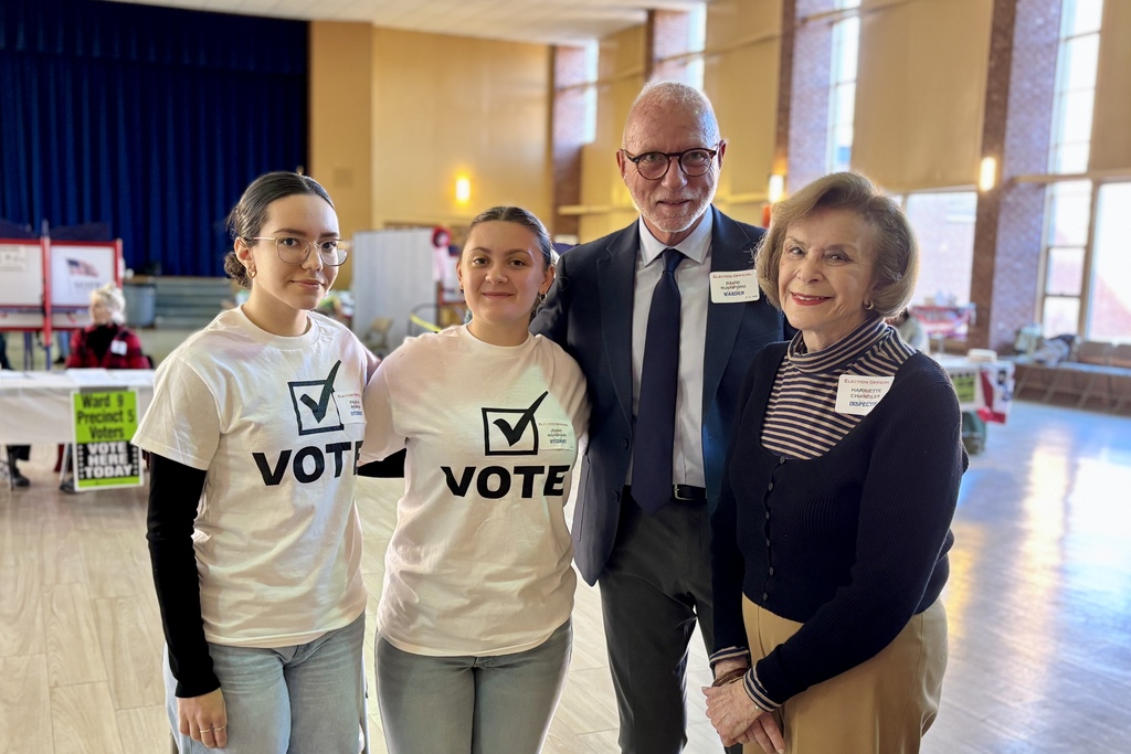 A group of people pose together, some wearing 'VOTE' shirts, at a polling location.