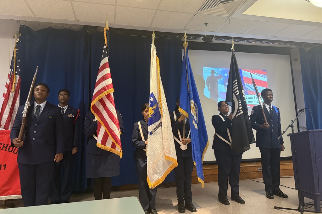 A group of students in uniform stand with flags in a presentation setting.