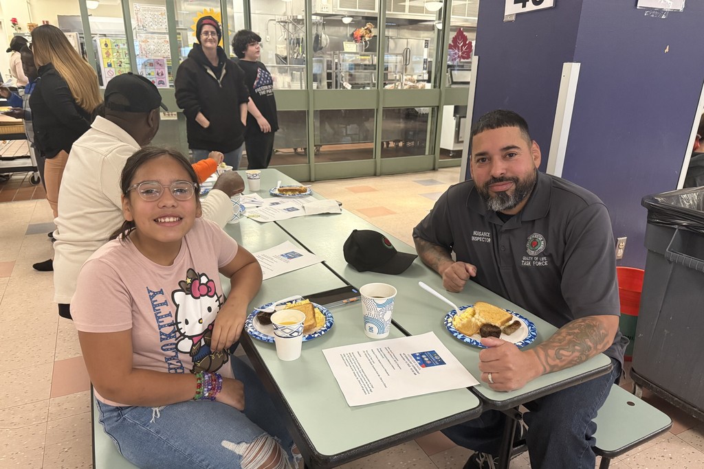 A young girl and a man smile at the camera while seated at a table with food.