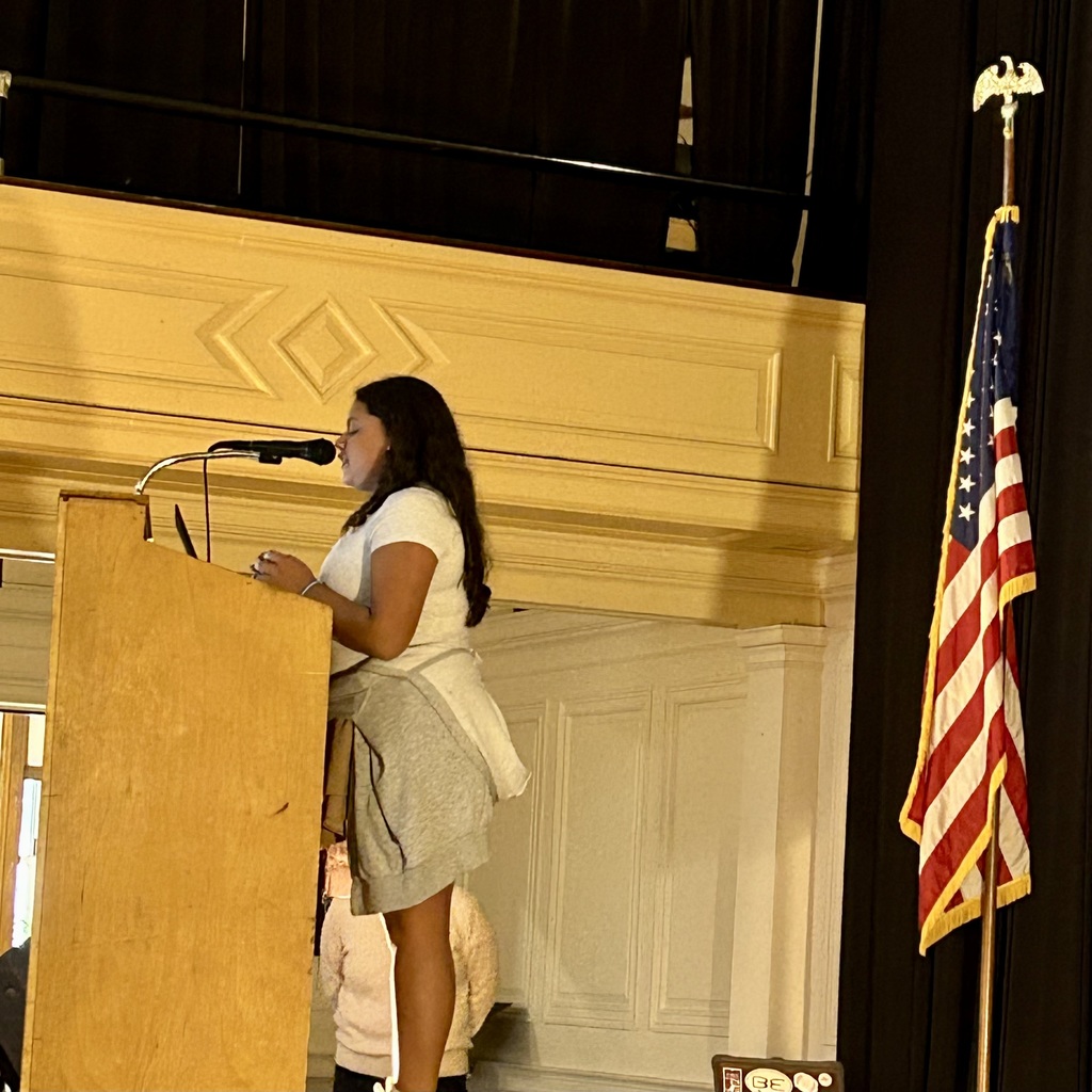 A young student speaks at a podium, microphone in front of her.