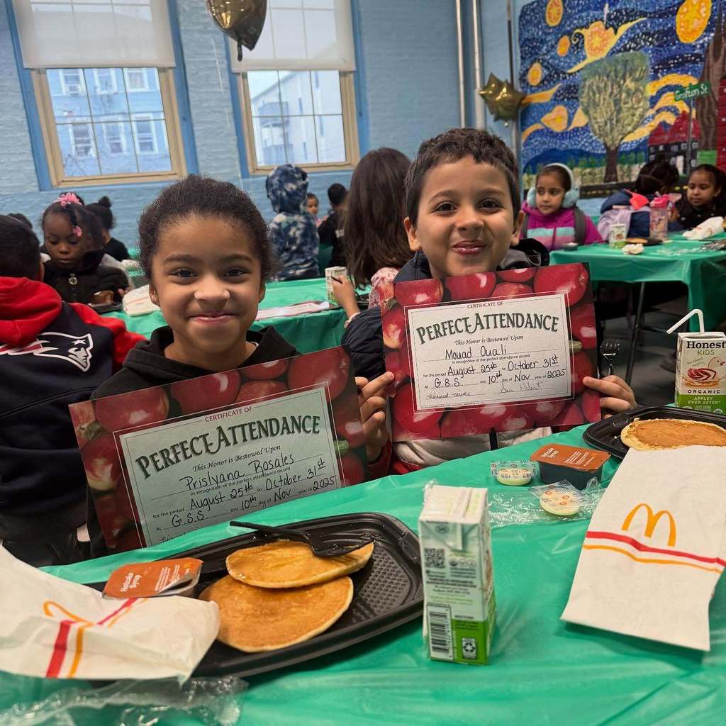 Two smiling children hold 'Perfect Attendance' certificates at a school event.