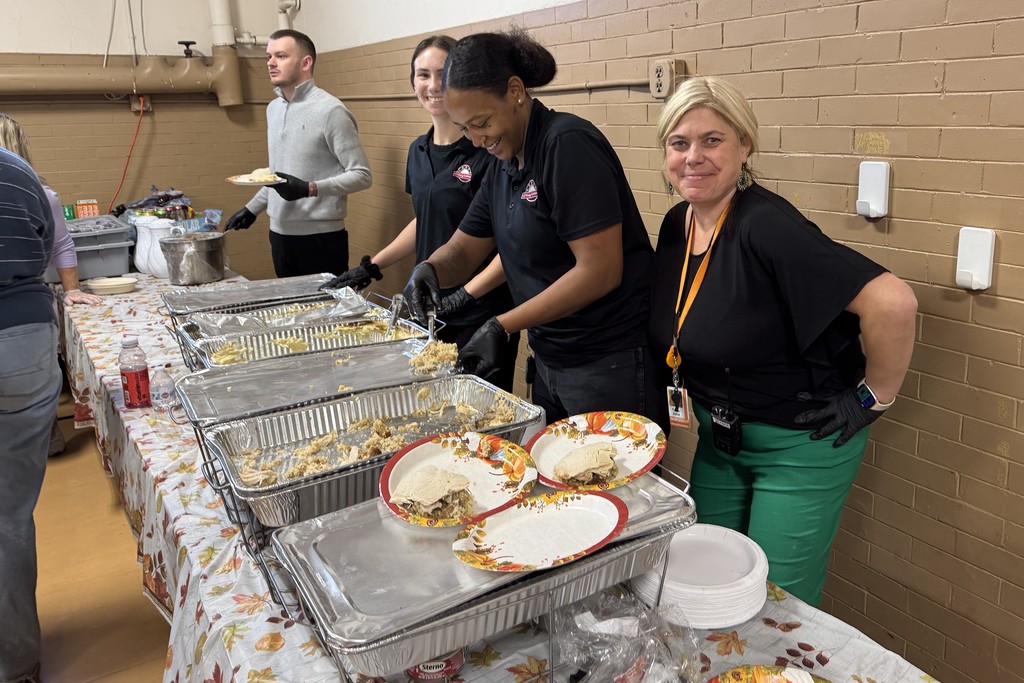 Volunteers serve food from warming trays at a community event.