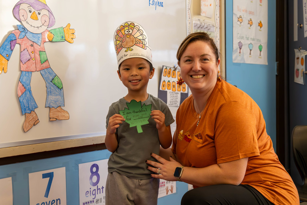 A smiling child and a woman pose together in a classroom setting.