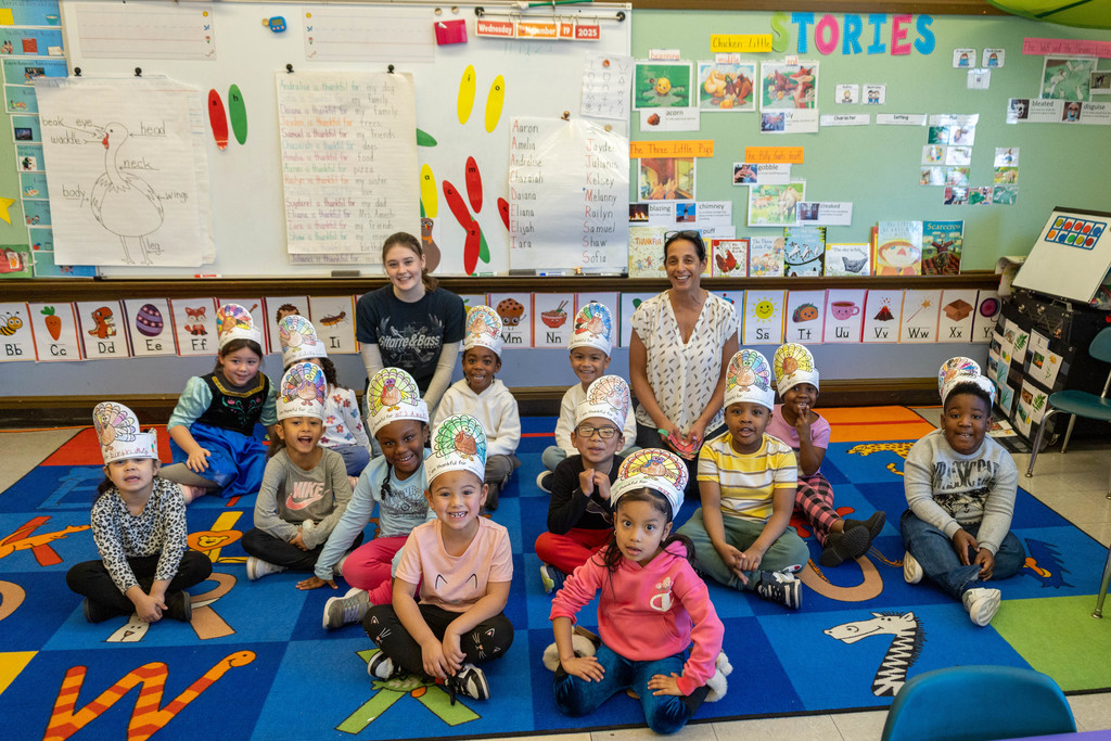 A classroom scene with children wearing turkey hats, smiling at the camera.