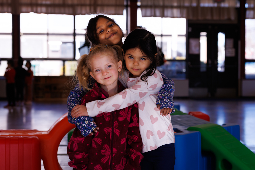 Three young students hug each other while smiling for a photo.