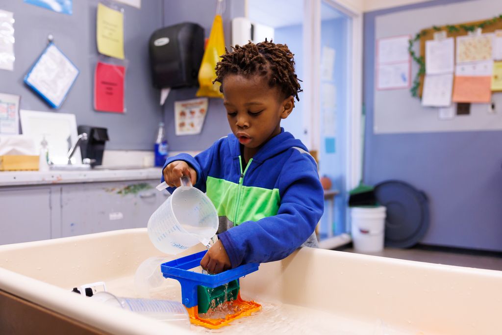 A young student is focused while playing at a water table.