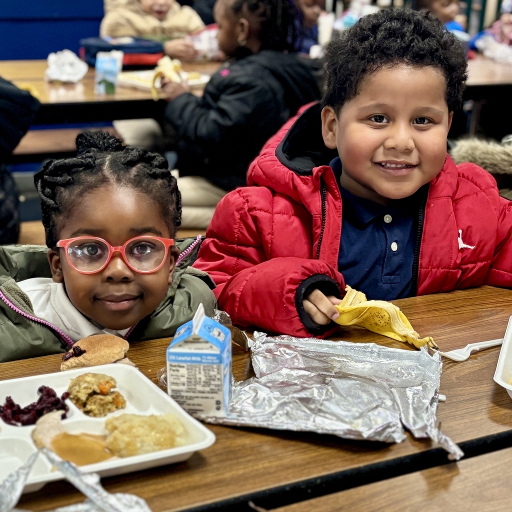 Two children smile at the camera while seated at a table with food.