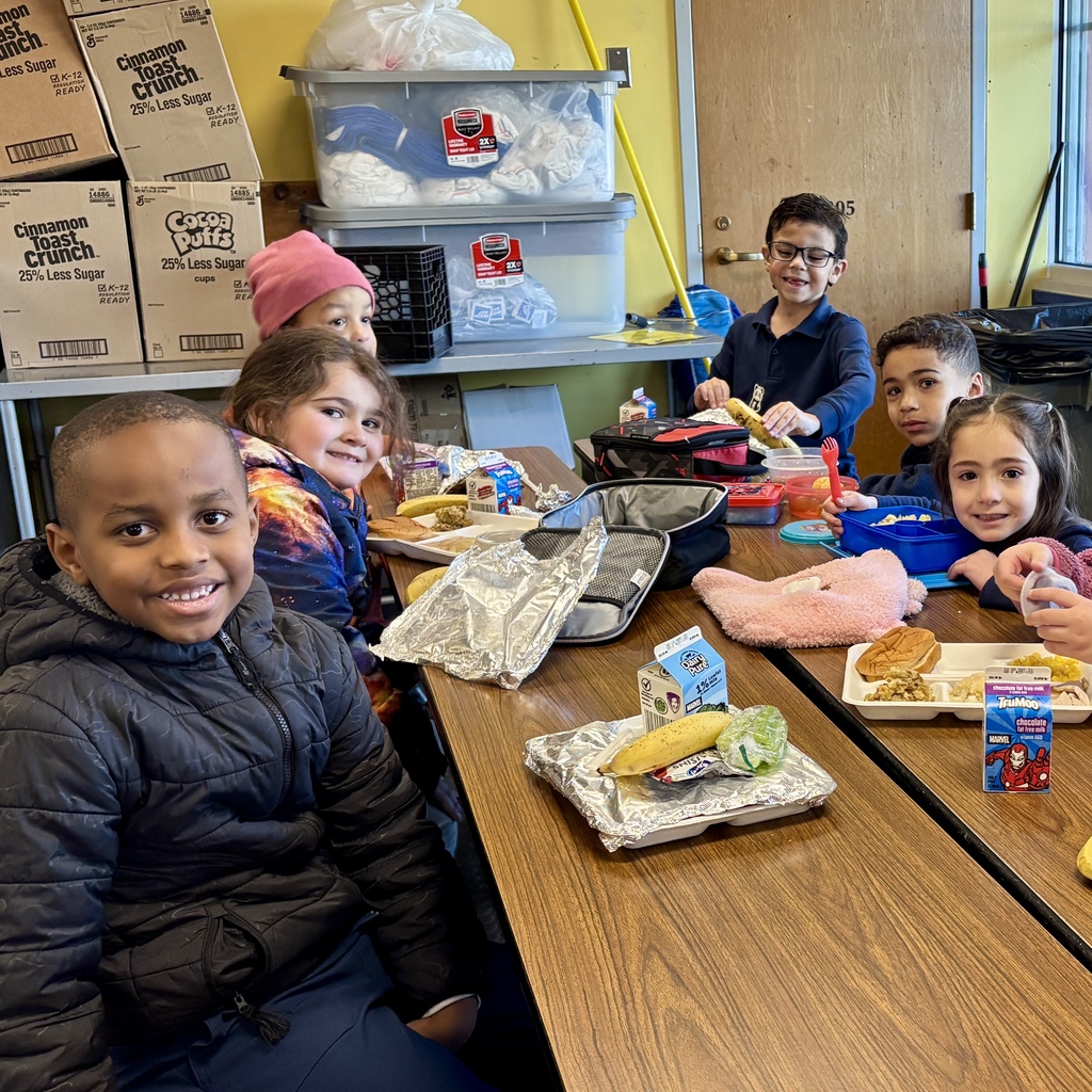 A group of children smile while eating lunch at a school table.