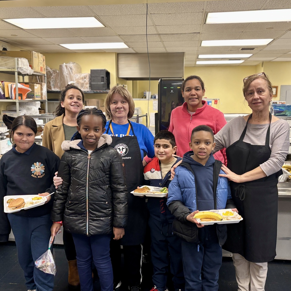 A group of adults and children pose together in a school cafeteria.