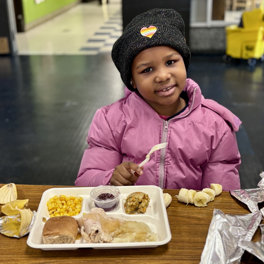 A young girl smiles while holding a fork, ready to eat her meal.