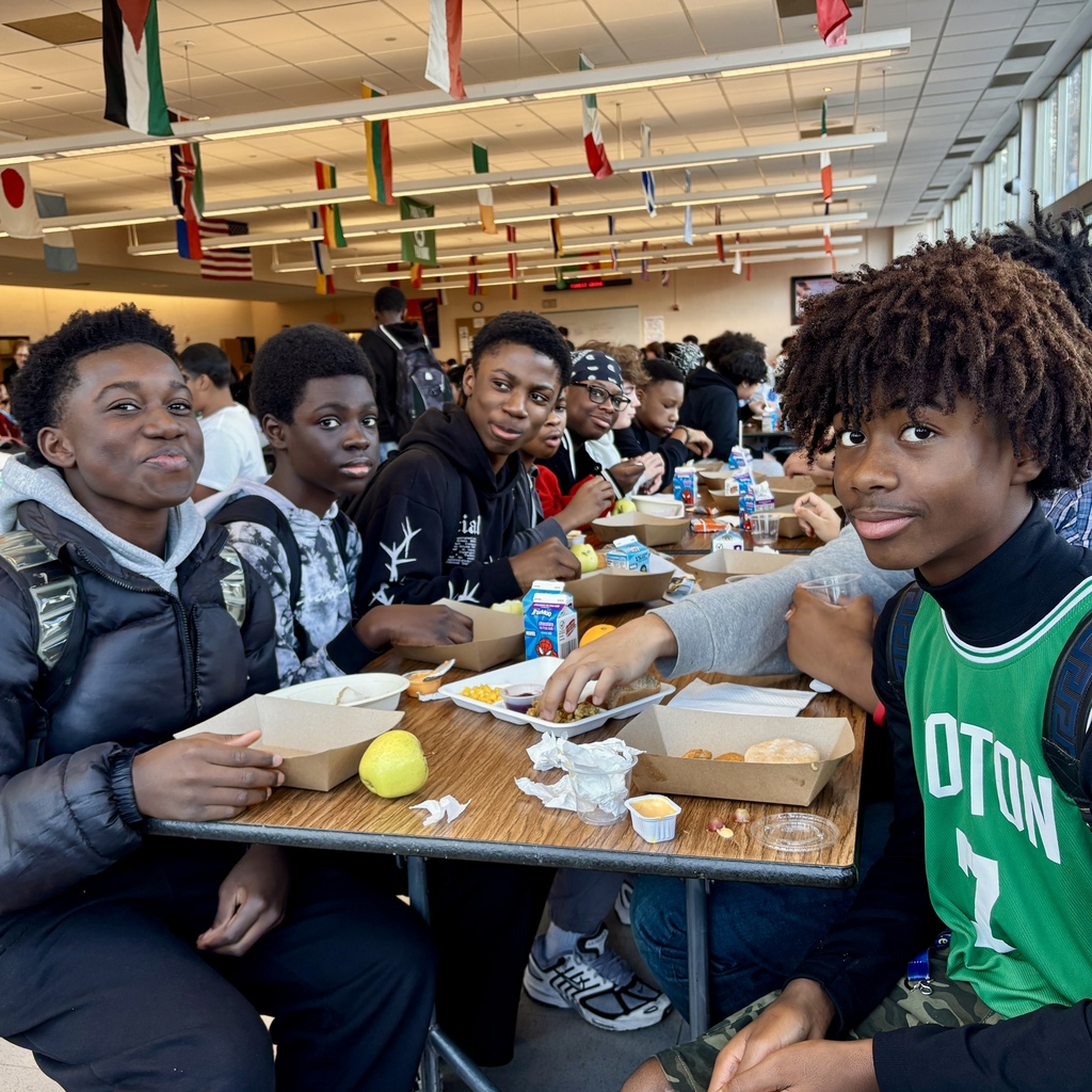A group of students sit at a table in a cafeteria, enjoying lunch.