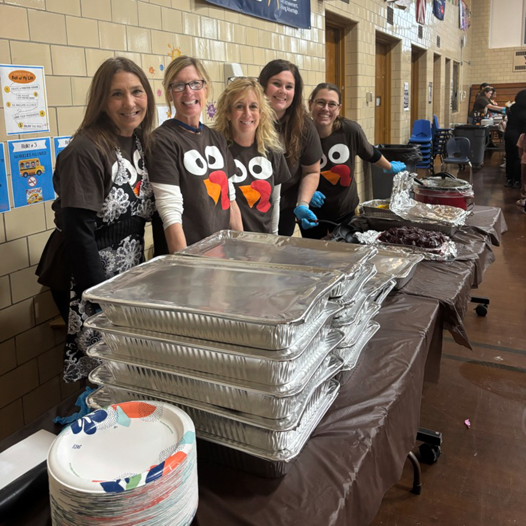 Staff members smile for a photo while standing behind a table of food.