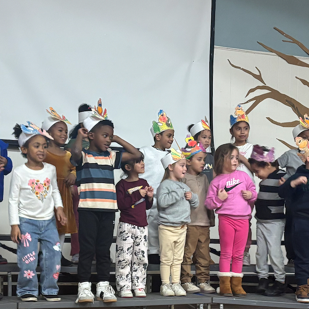 Students perform on stage while wearing turkey hats.