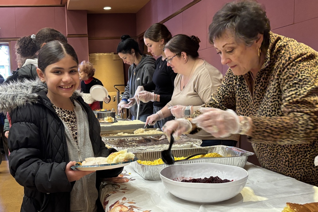 A young girl smiles while holding a plate of food at a serving table.
