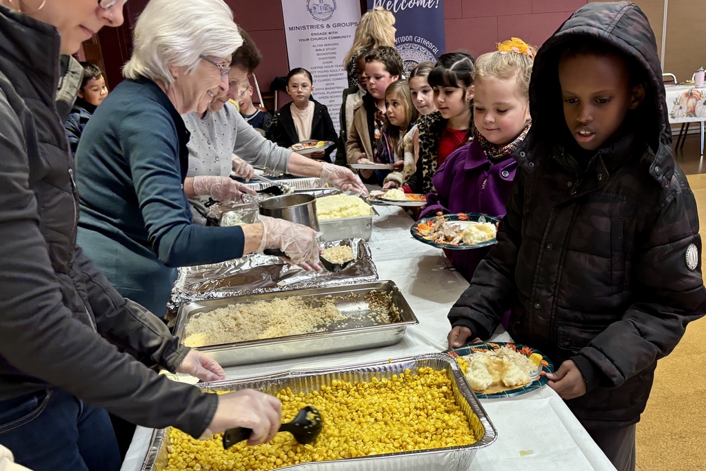 People serve food to children at a community event, with various dishes available.