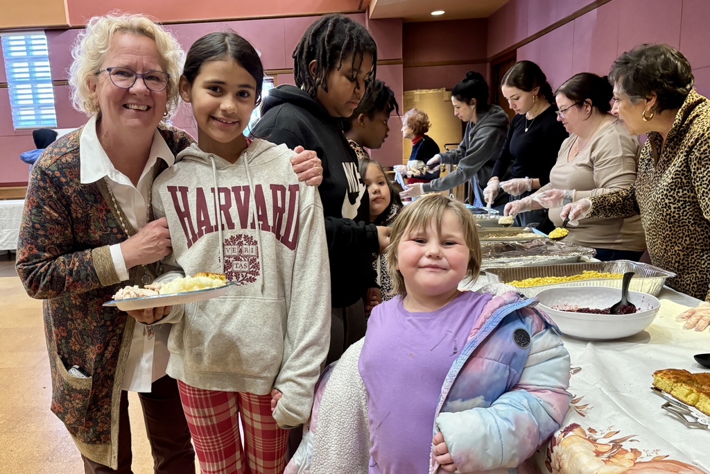 A group of people gather around a table, some holding plates of food, smiling.