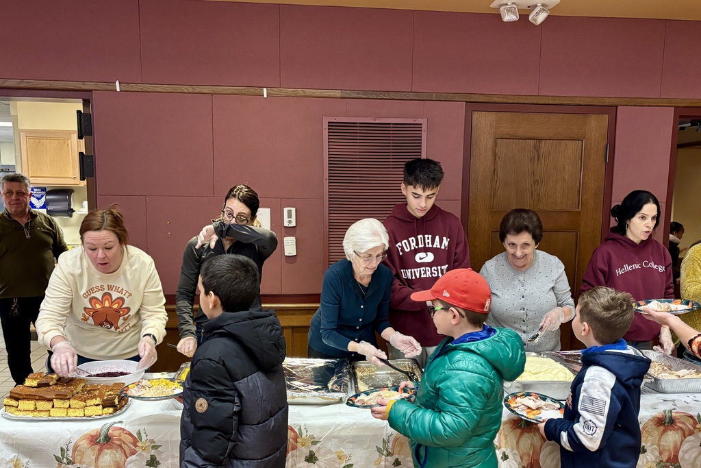 People serve food at a community gathering, with various dishes on display.