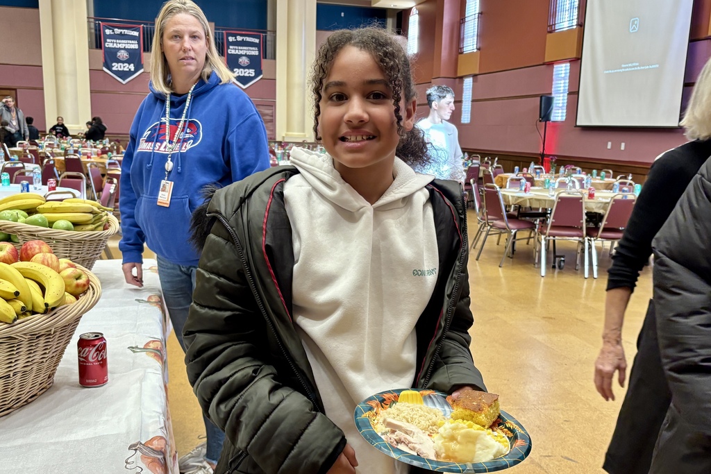 A young girl smiles, holding a plate of food at an event.