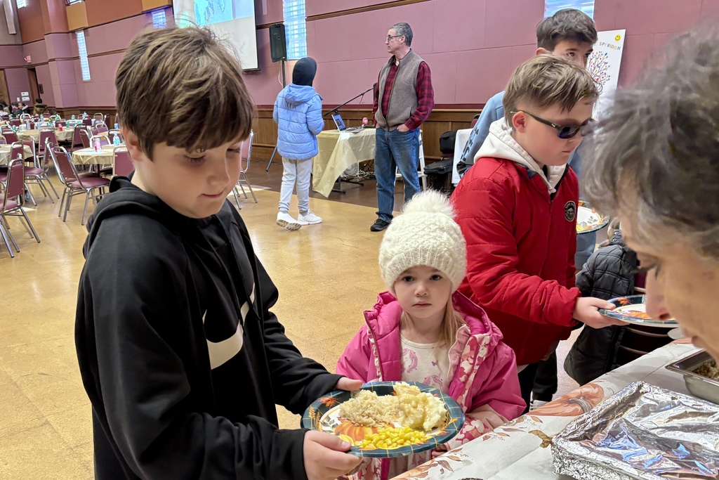 Children and adults gather at a food service area, likely at an event.