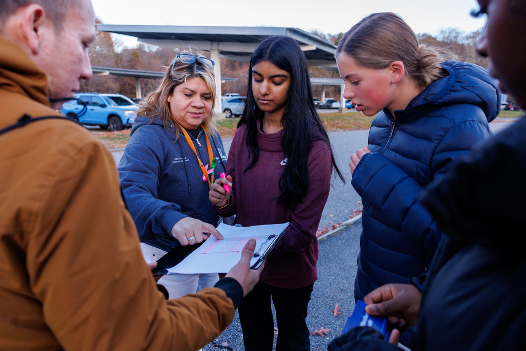 A teacher and two students help an adult during a donation event.