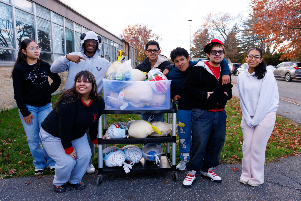 Seven students stand in front of a cart full of frozen turkeys during a donation event.
