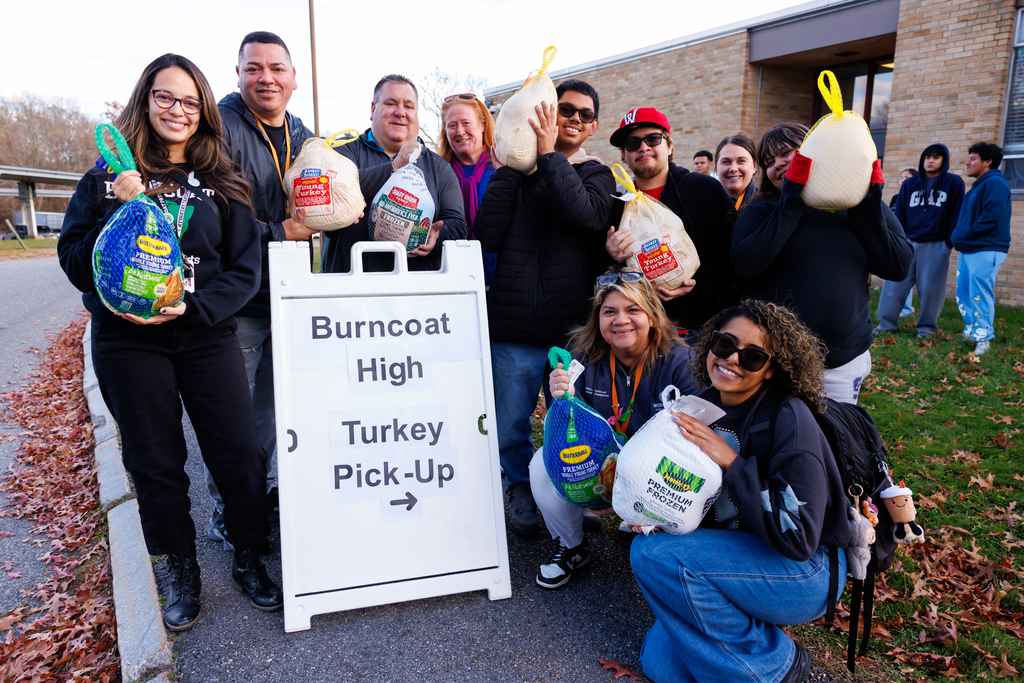 Nine students and staff stand in front of a sign that says "Burncoat High Turkey Pick Up" while holding turkeys.