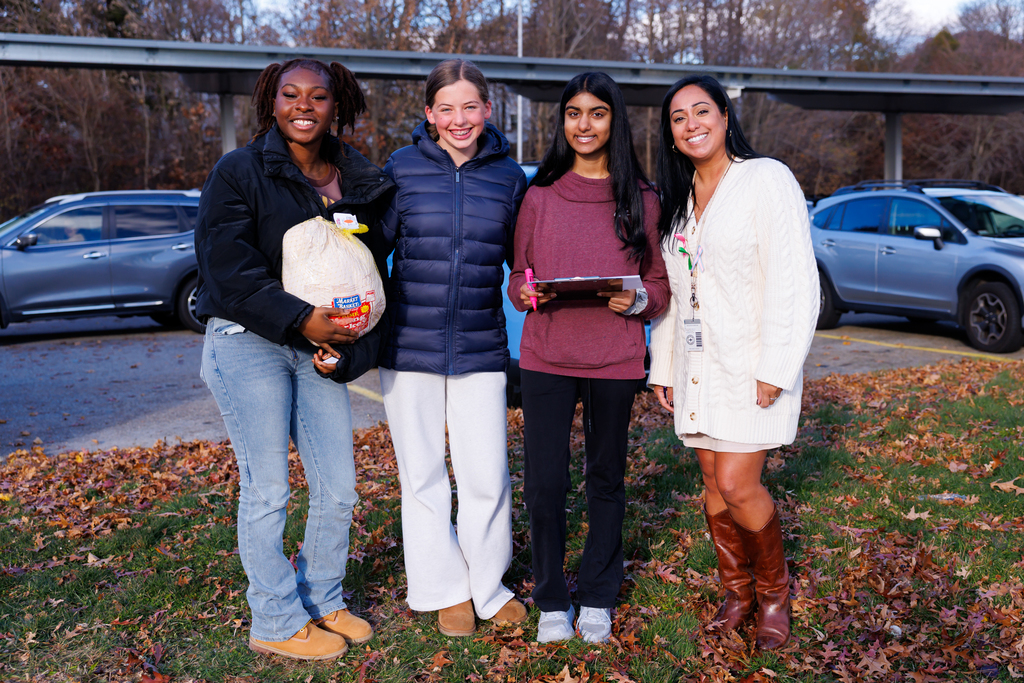 Three students and a staff member stand together for a photo on the grass, one of them is holding a turkey.
