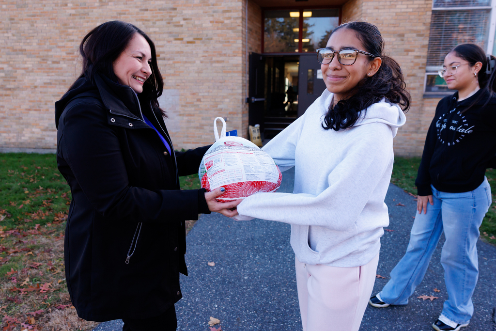 A student hands over a turkey to an adult during a donation event.