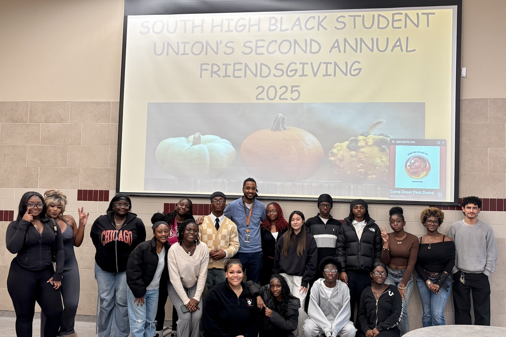 A group of diverse students pose together in front of a Friendsgiving banner.
