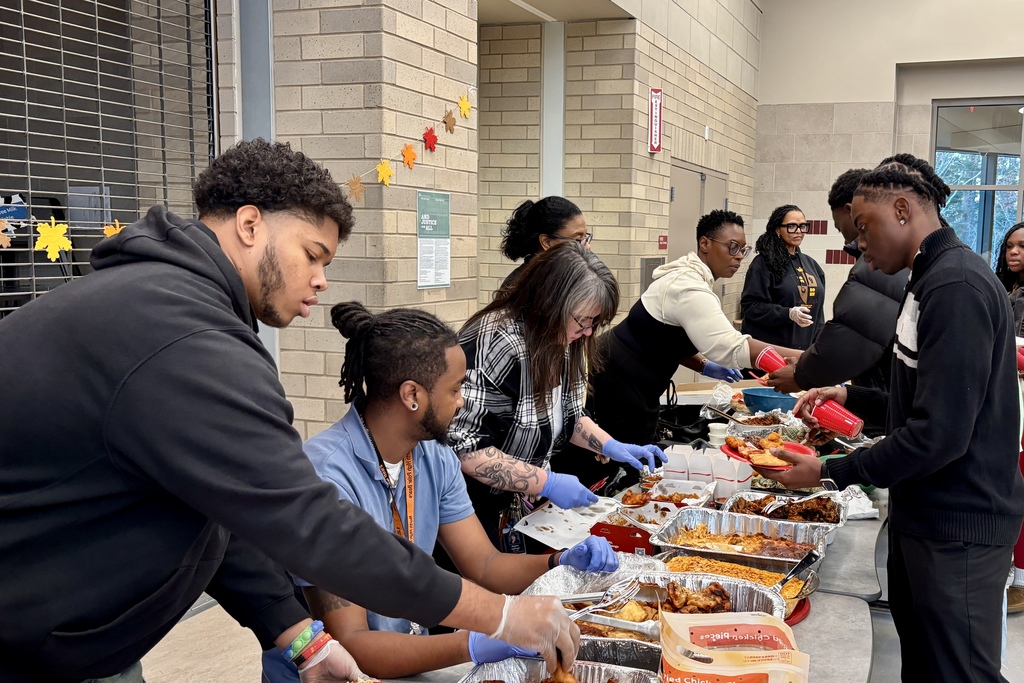 People serve food from trays at a community gathering, with a variety of dishes.