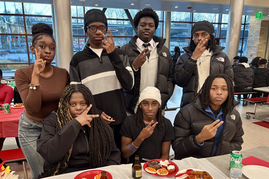 A group of young people pose for a photo indoors, some making peace signs.
