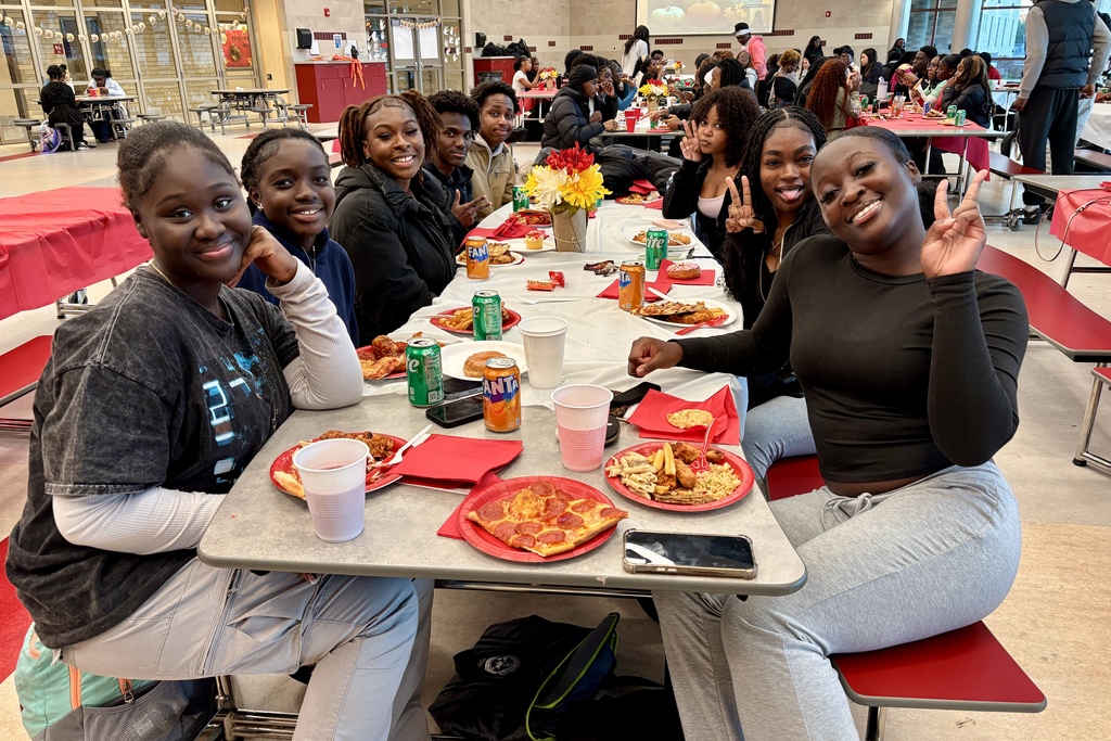 A group of friends smiles at the camera while enjoying a meal together.