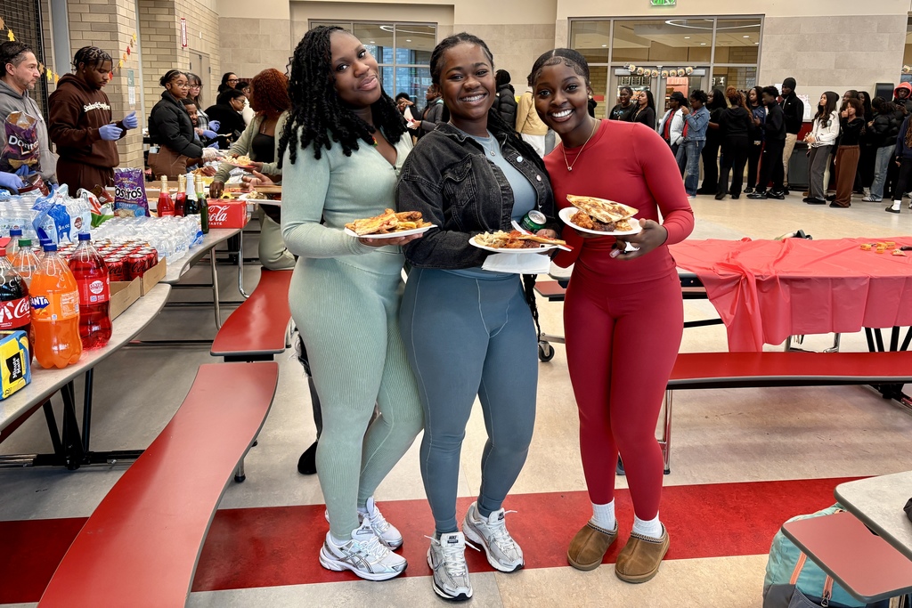 Three young women smile, holding plates of food at a gathering.
