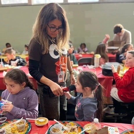 A woman holds a microphone for a young girl at a school event.