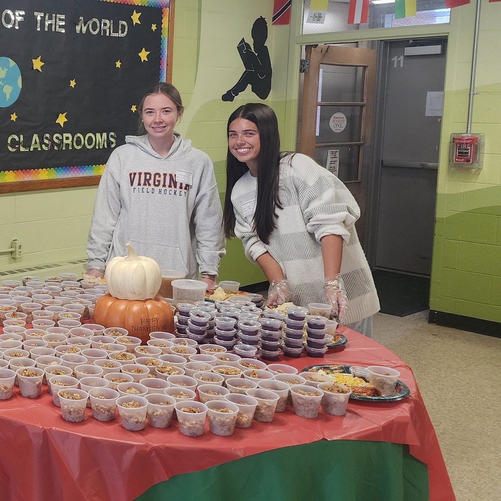 Two young women stand behind a table laden with food, smiling at the camera.